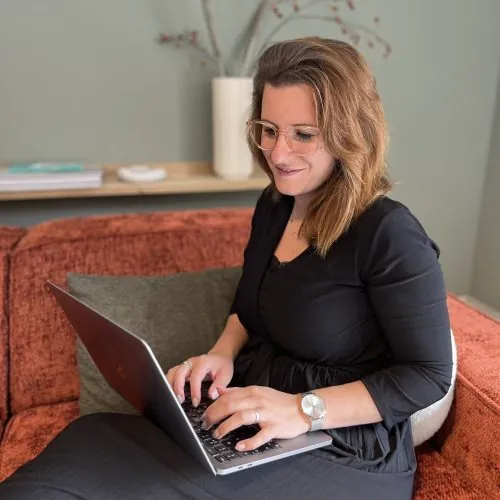 Misha van der Zee werkt op haar laptop op een bank